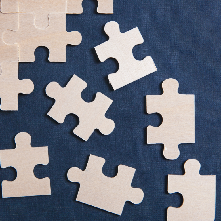 Scattered wooden puzzle pieces on a dark blue surface, symbolising problem-solving, strategy, and finding the missing link.