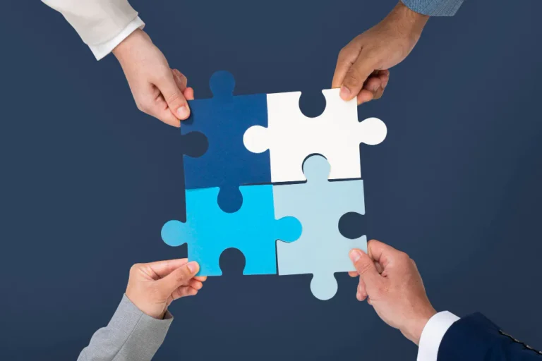 Four business professionals joining blue puzzle pieces, symbolising collaboration, connected data, strategic alignment and a unified approach to B2B marketing and revenue growth.