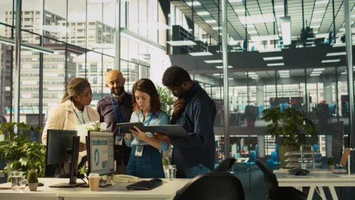 A diverse B2B marketing team collaborates around laptops and digital dashboards in a modern office, reviewing data, strategy and campaign performance.